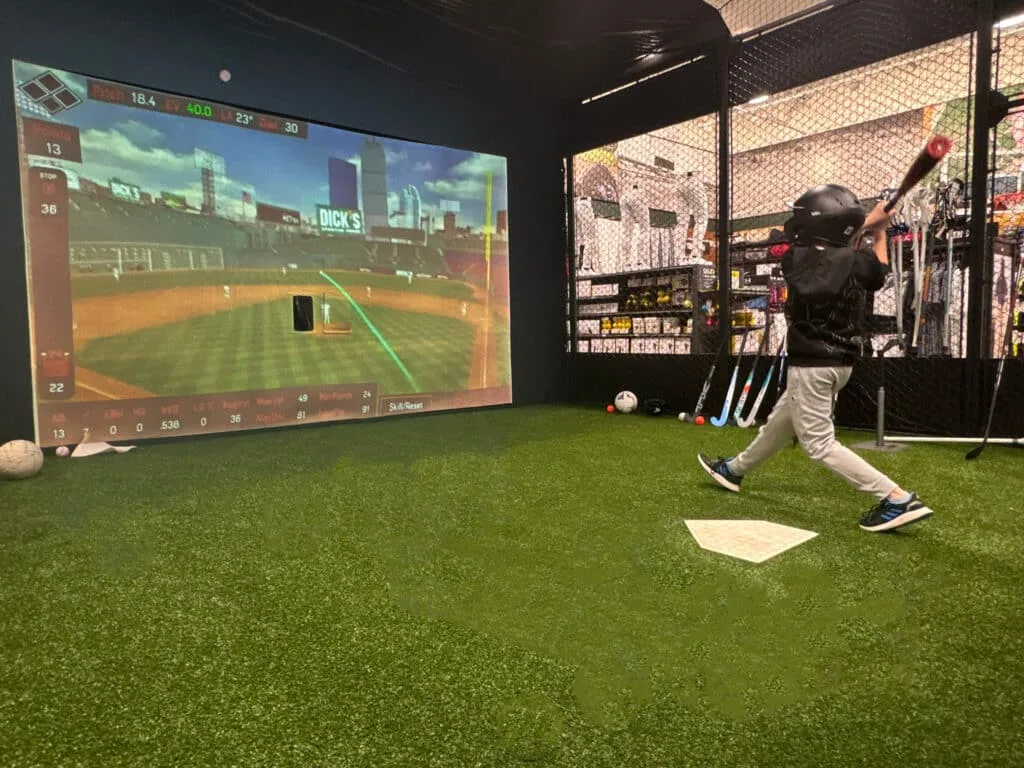 Young player swinging in a HitTrax simulator cage